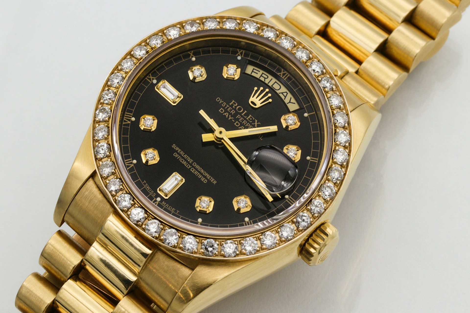 Close-up of a gold Rolex Day-Date watch with a black dial, diamond hour markers, and a gold bracelet, displayed on a white surface.