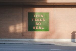 Green square mural on a brick wall reading: THIS FEELS SO REAL.