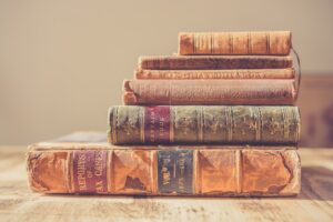 Stack of six vintage leather-bound books with worn spines on a wooden table.